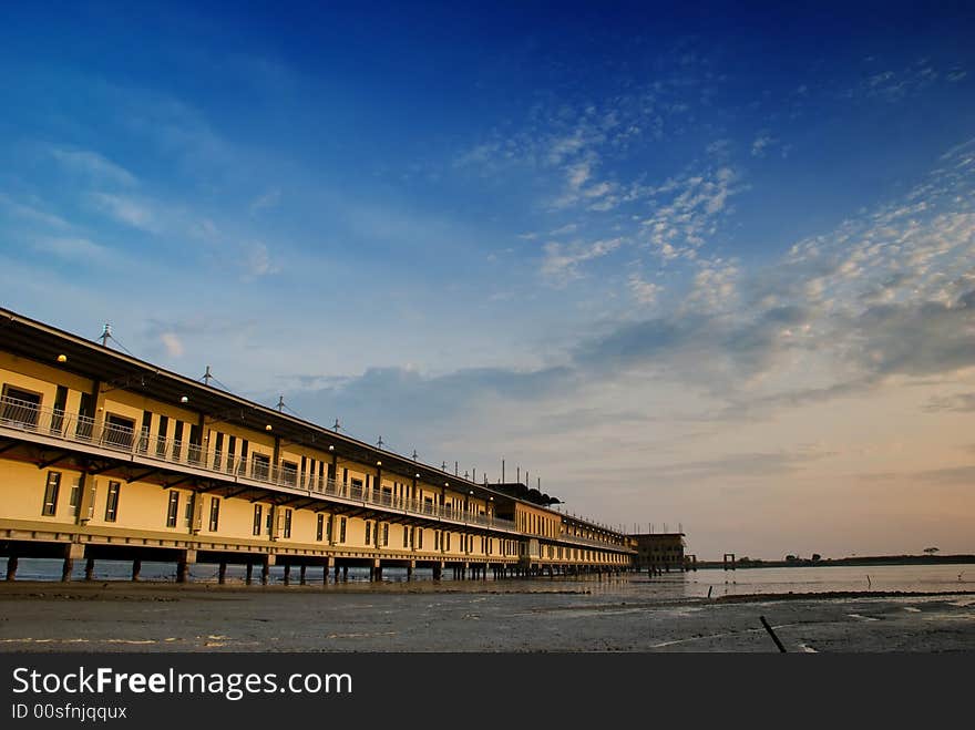 Long linear building on stilts built over muddy flats as a beach resort as seen at low tide and at sunset. Long linear building on stilts built over muddy flats as a beach resort as seen at low tide and at sunset