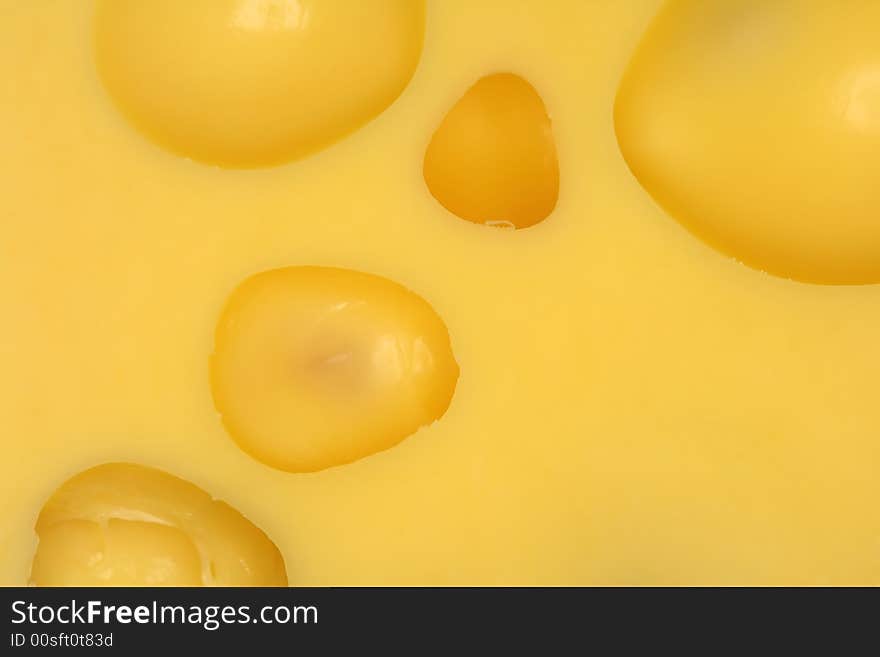 An extreme close-up of yellow cheese with big wholes.