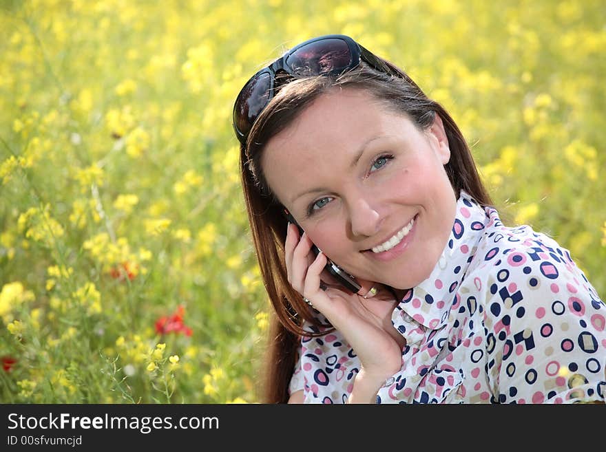 Pretty young woman talking on mobile phone on a meadow smiling