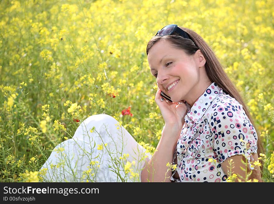 Pretty young woman talking on mobile phone on a meadow smiling