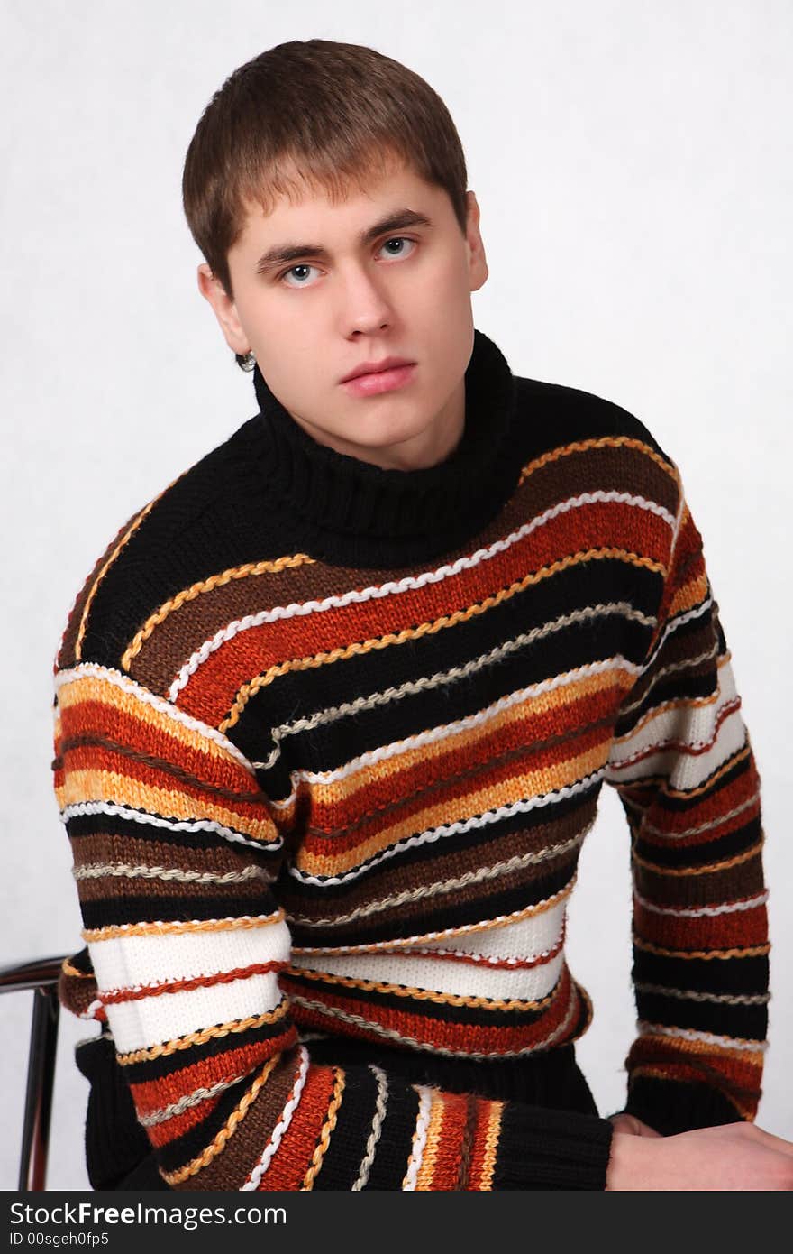 Portrait of the young guy in jeans and a sweater sitting on a chair. Portrait of the young guy in jeans and a sweater sitting on a chair