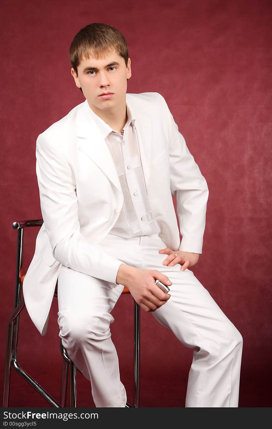 The portrait of the guy sitting on a chair in a white suit which holds a mobile phone tube in the right hand. The portrait of the guy sitting on a chair in a white suit which holds a mobile phone tube in the right hand