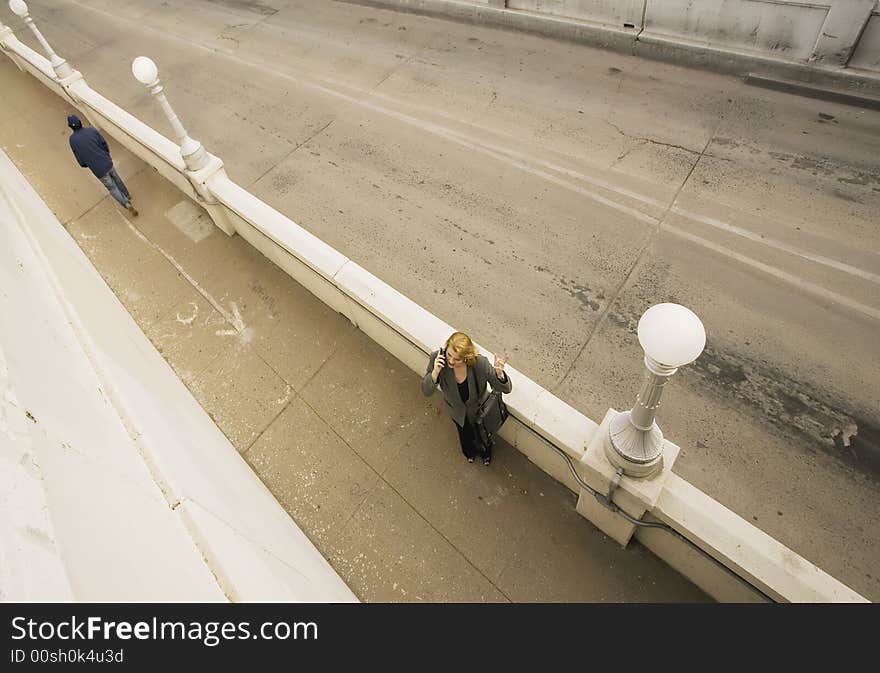 Wide shot from above of  woman on her cell phone next to an empty road. Wide shot from above of  woman on her cell phone next to an empty road.