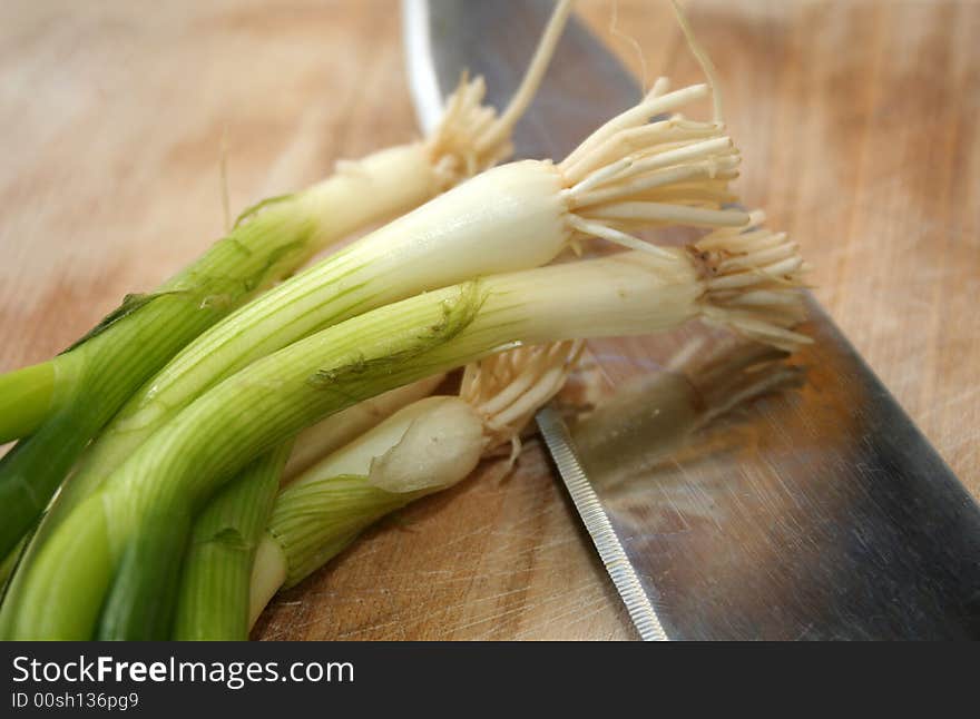 A group of fresh green onions sit close to a knife on a cutting board. A group of fresh green onions sit close to a knife on a cutting board.