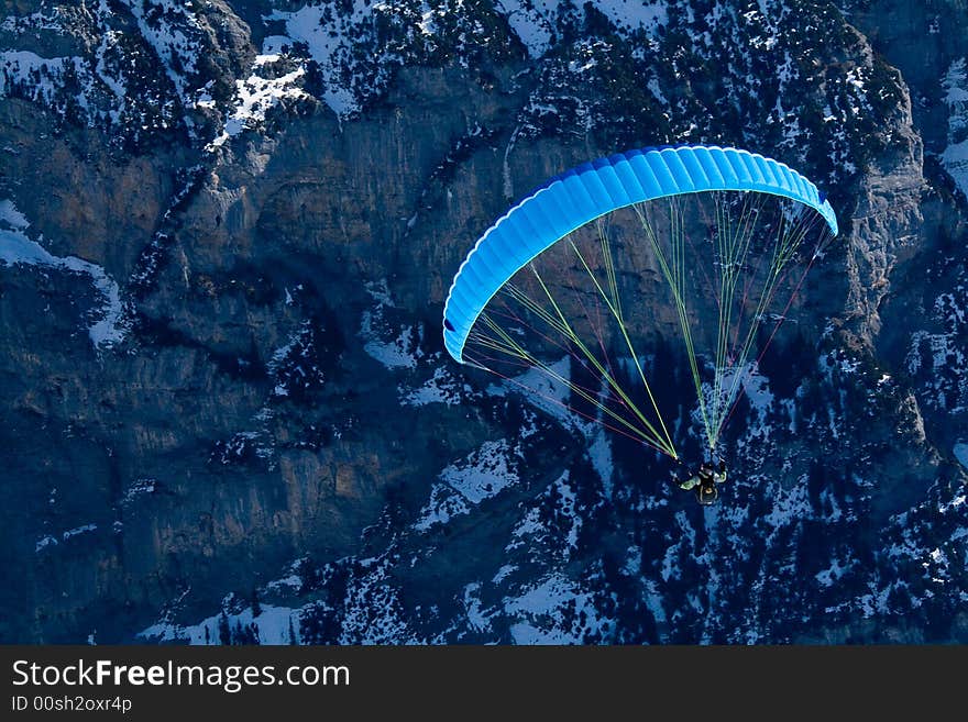 Paraglider with a blue parachute going towards the rocks. Swiss Alps. Paraglider with a blue parachute going towards the rocks. Swiss Alps.