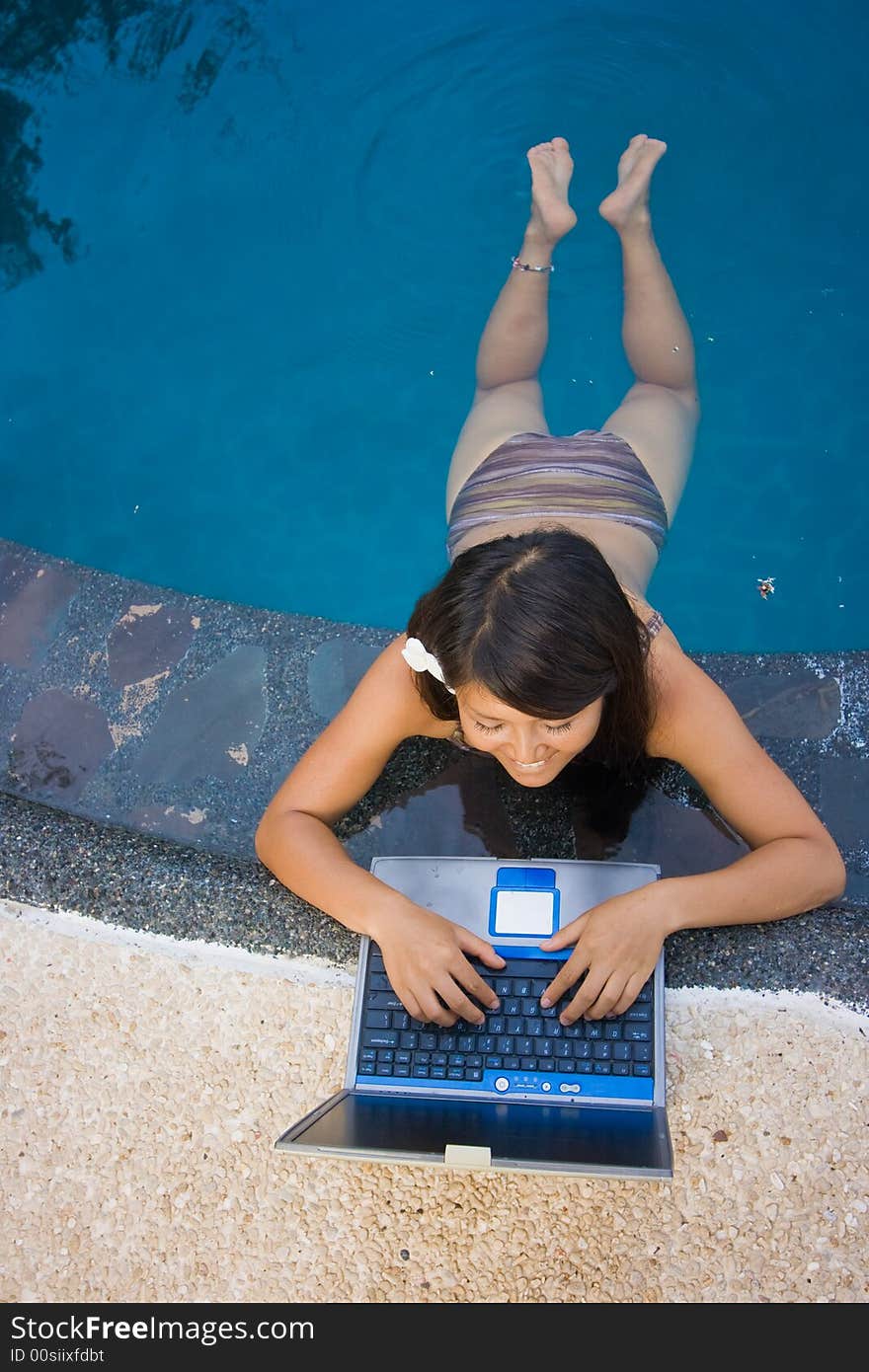 Attractive young Asian business woman working remotely on a laptop computer beside an infinity pool at a private tropical resort paradise vacation. Room for text. Attractive young Asian business woman working remotely on a laptop computer beside an infinity pool at a private tropical resort paradise vacation. Room for text.