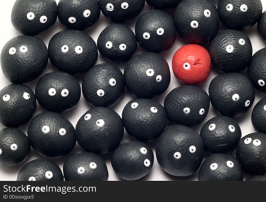 The idea of being different, distinguished among the others. Little plasticine balls with eyes. The red one is winking. White background. The idea of being different, distinguished among the others. Little plasticine balls with eyes. The red one is winking. White background.