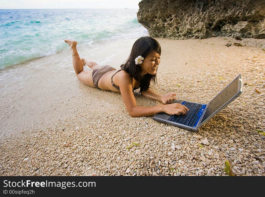 Attractive young Asian business woman working remotely on a laptop computer at a private white sand beach beside the sea in the surf at a tropical resort paradise vacation. Room for text. Attractive young Asian business woman working remotely on a laptop computer at a private white sand beach beside the sea in the surf at a tropical resort paradise vacation. Room for text.