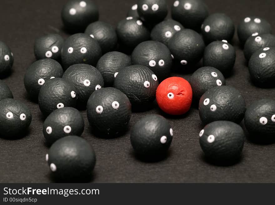 The idea of being different, distinguished among the others. Little plasticine balls with eyes. The red one is winking. Black background. The idea of being different, distinguished among the others. Little plasticine balls with eyes. The red one is winking. Black background.