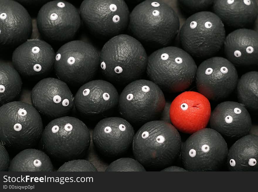 The idea of being different, distinguished among the others. Little plasticine balls with eyes. The red one is winking. Black background. The idea of being different, distinguished among the others. Little plasticine balls with eyes. The red one is winking. Black background.