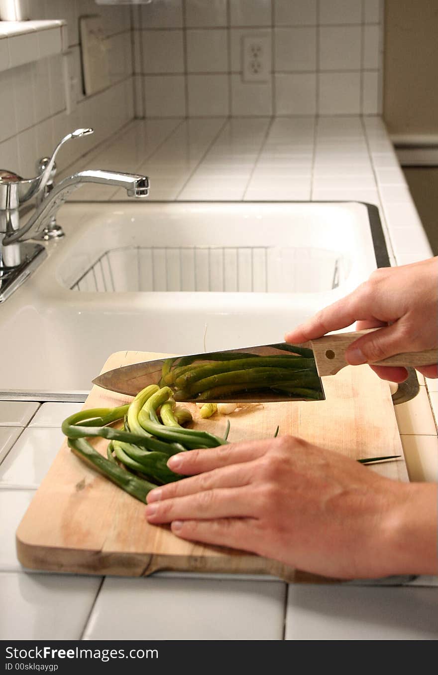 A person cuts fresh green onions on a wooden cutting board in the kitchen. A person cuts fresh green onions on a wooden cutting board in the kitchen.