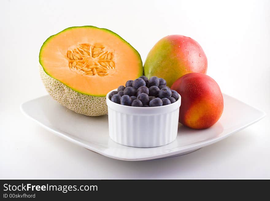 Cantaloupe,blueberries,mango and a nectarine share space on a white plate. Cantaloupe,blueberries,mango and a nectarine share space on a white plate.