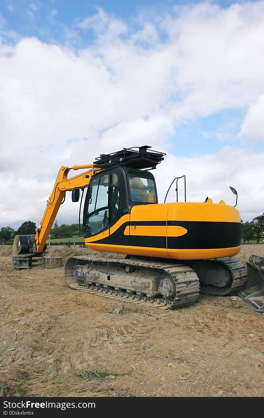 Rear view of a yellow industrial digger standing idle on rough ground. Rear view of a yellow industrial digger standing idle on rough ground.