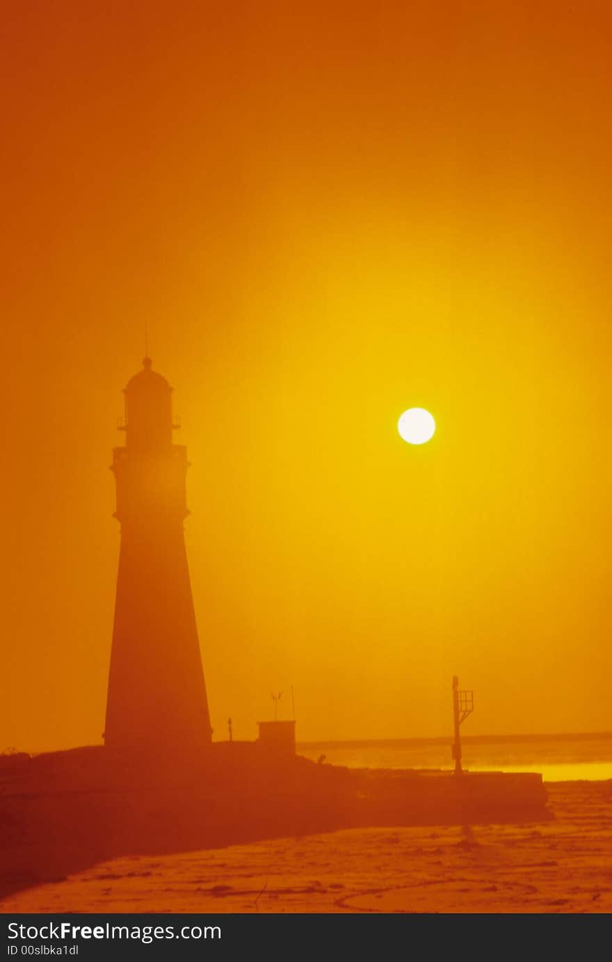 A lighthouse is engulfed by the orange glow of the sun through the fog. A lighthouse is engulfed by the orange glow of the sun through the fog