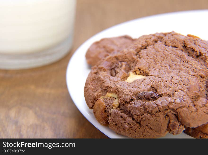 A plate of chocolate cookies with a glass of milk in the background. A plate of chocolate cookies with a glass of milk in the background.