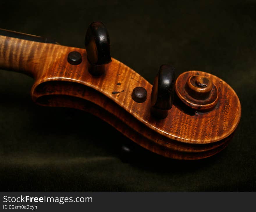 Close-up of violin scroll and pegbox, with part of neck... on dark green velvet. Close-up of violin scroll and pegbox, with part of neck... on dark green velvet