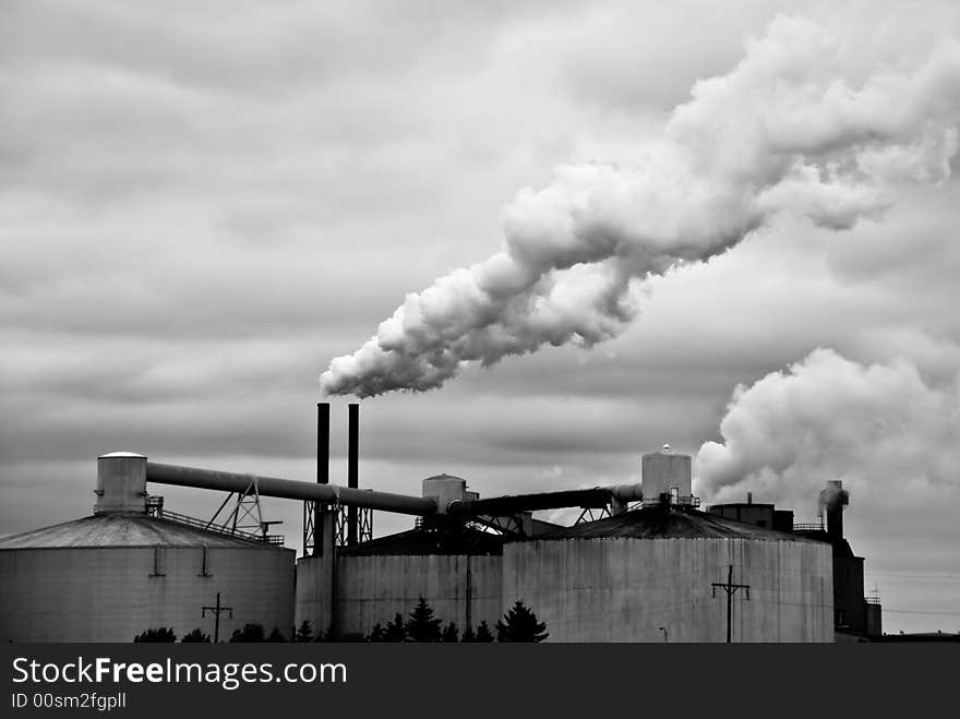 Huge factory spews smoke from its towers into a cloudy sky. Huge factory spews smoke from its towers into a cloudy sky