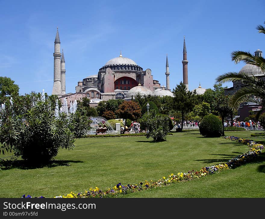 Byzantine landmark church Hagia Sophia converted to a mosque by the Ottomans behind trees, green grass, and colorful pansies, in Istanbul under blue sky. Byzantine landmark church Hagia Sophia converted to a mosque by the Ottomans behind trees, green grass, and colorful pansies, in Istanbul under blue sky