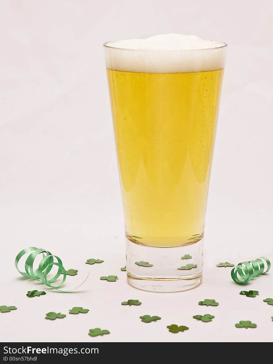 A tall glass of beer against a white background with shamrock confetti around it. A tall glass of beer against a white background with shamrock confetti around it