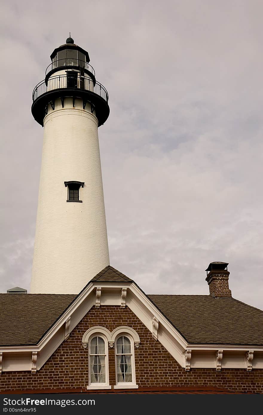 A white lighthouse behind a brick house with cloudy sky. A white lighthouse behind a brick house with cloudy sky