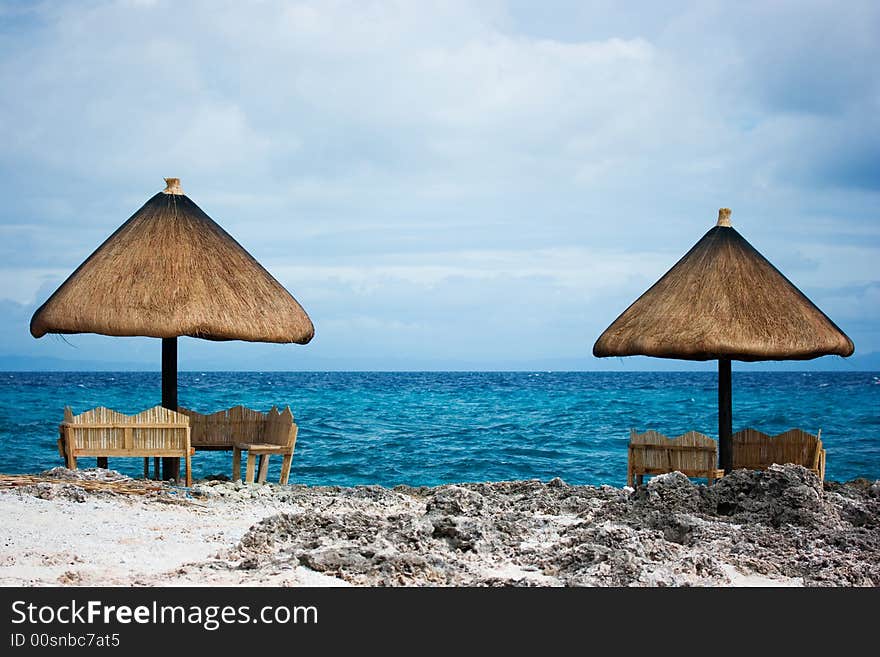 Relaxing native style cabanas on a white sand tropical beach beside the ocean of Caribbean blue water with white foamy waves crashing. Relaxing native style cabanas on a white sand tropical beach beside the ocean of Caribbean blue water with white foamy waves crashing