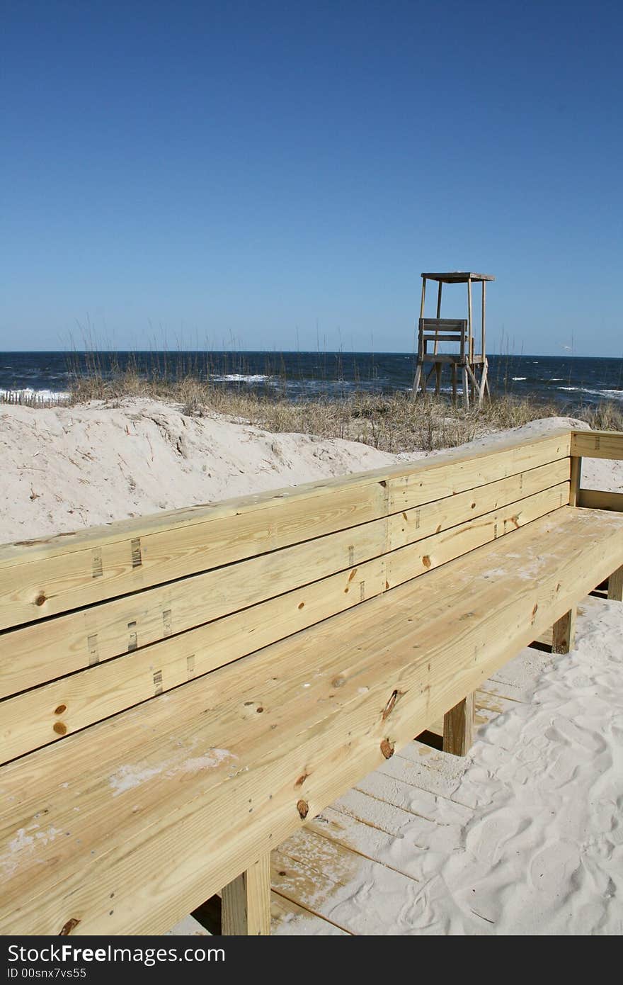 A wood bench along the path to the beach. Lifeguard hut in background. A wood bench along the path to the beach. Lifeguard hut in background.