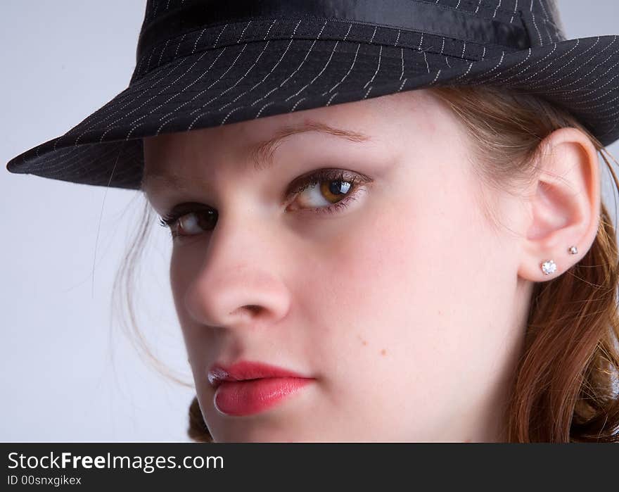 Serious teen peering out from under the brim of her pin-striped fedora hat. Serious teen peering out from under the brim of her pin-striped fedora hat.