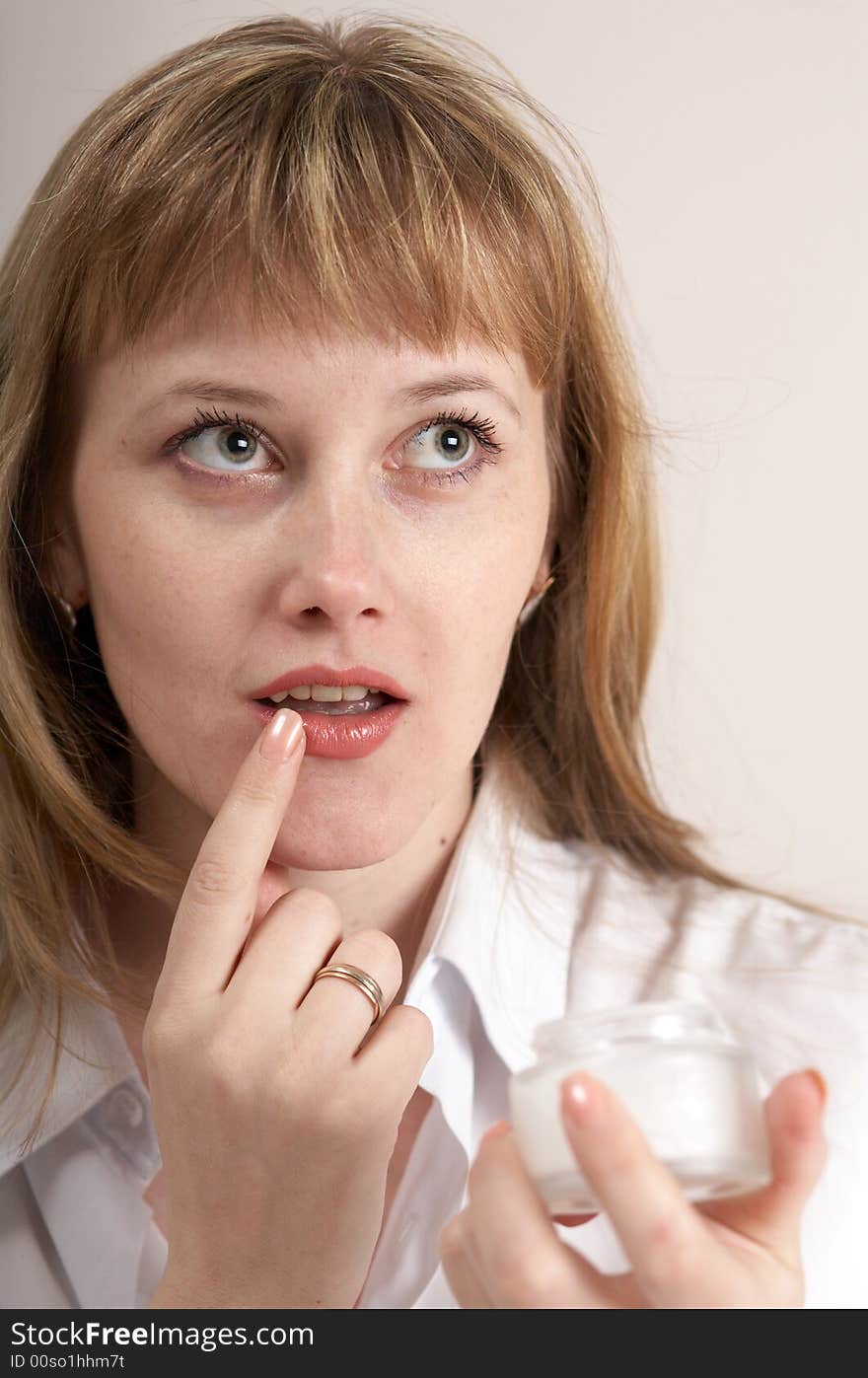 A girl spreading cream onto her lips. A girl spreading cream onto her lips