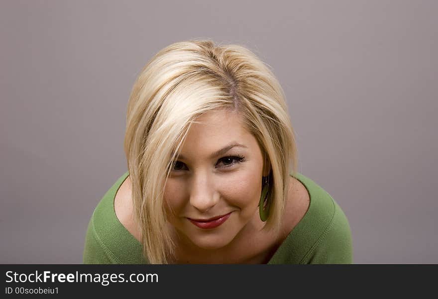 A blonde girl in a green blouse with her head bowed smiling at camera. A blonde girl in a green blouse with her head bowed smiling at camera