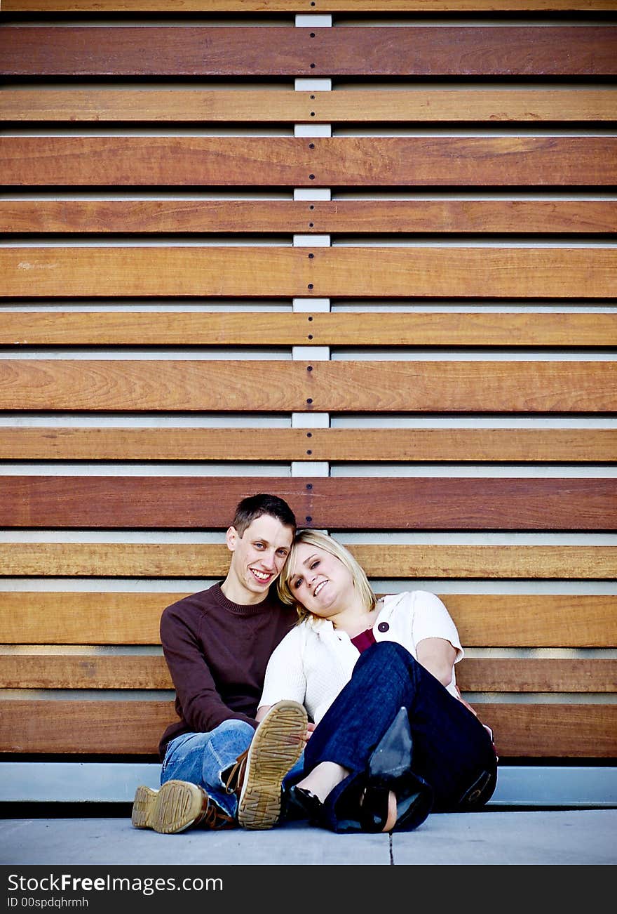 Young couple cuddling in front of a wall made of wood slats. Young couple cuddling in front of a wall made of wood slats