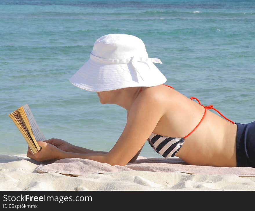 Woman in the swimming suit reads a book on the beach.