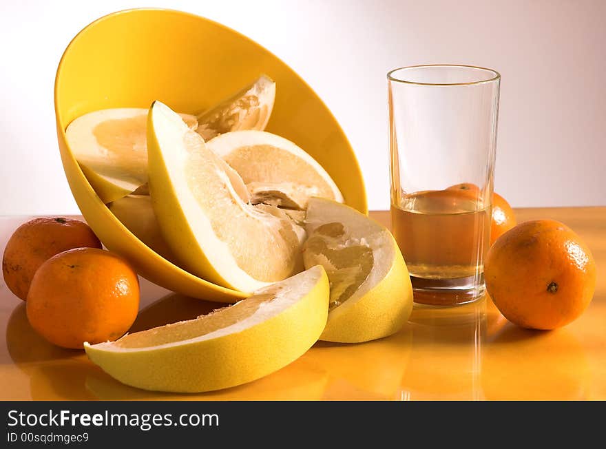 Citruses and glass of juice on yellow