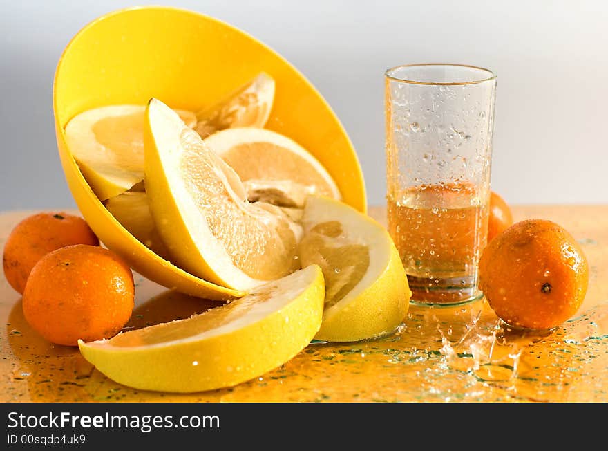 Citruses and glass of juice on yellow