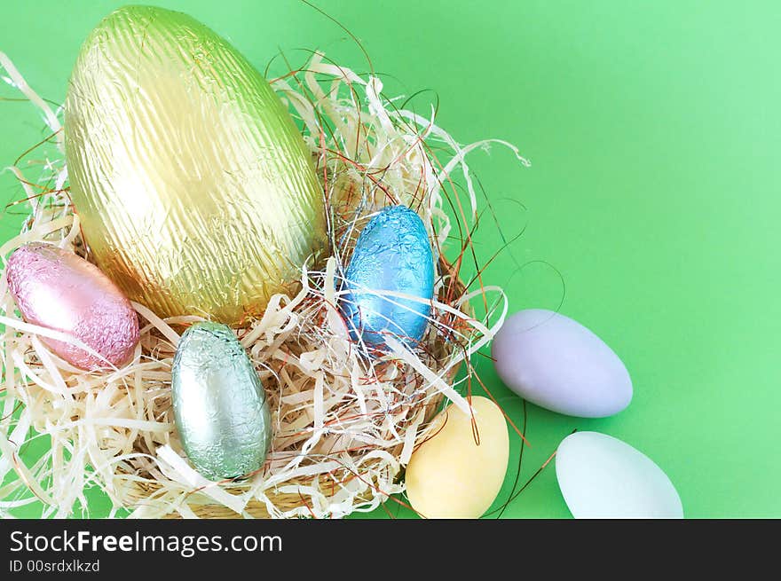 Chocolate Easter eggs in straw on green background