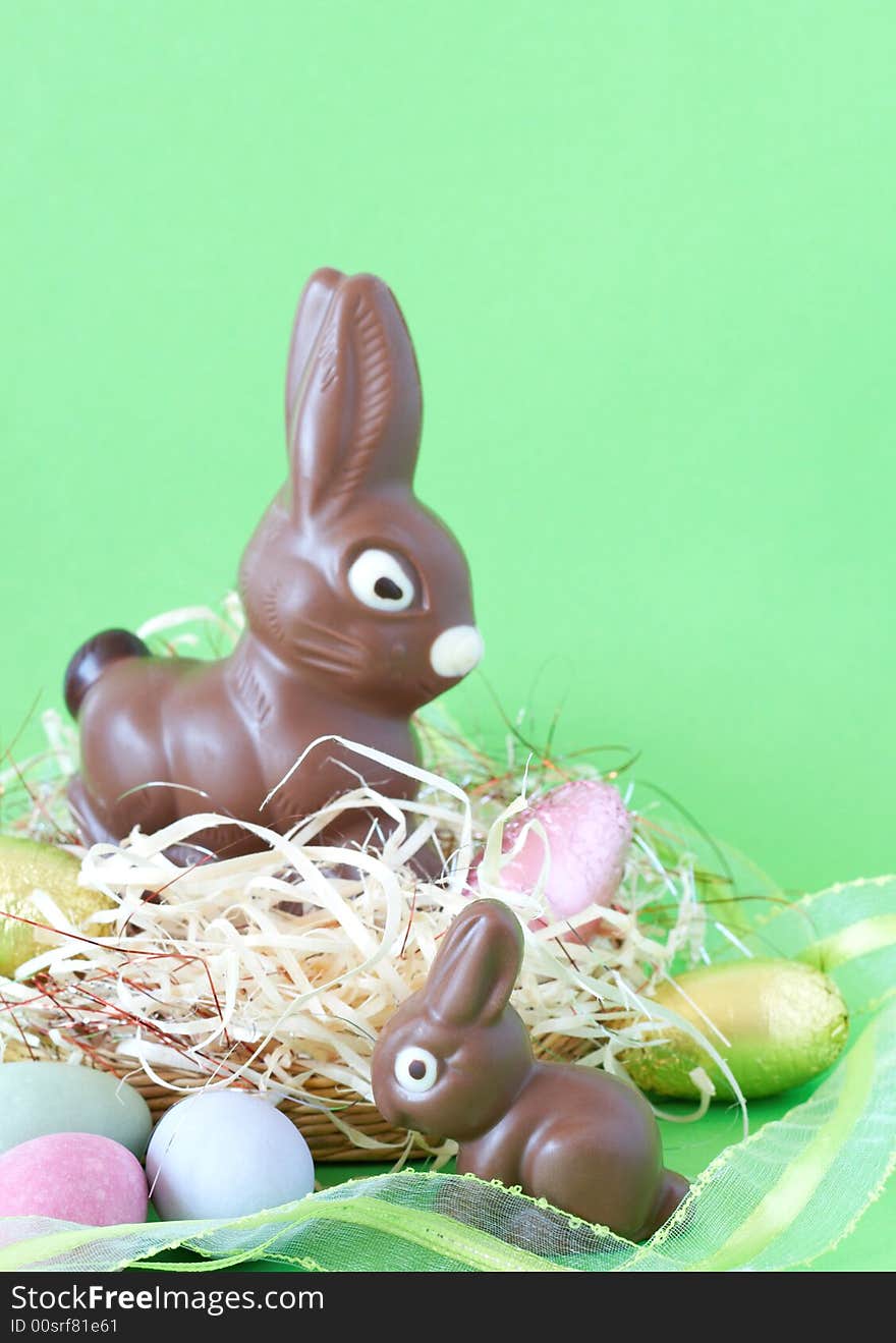 Two chocolate Easter bunnies with colorful chocolate eggs in straw