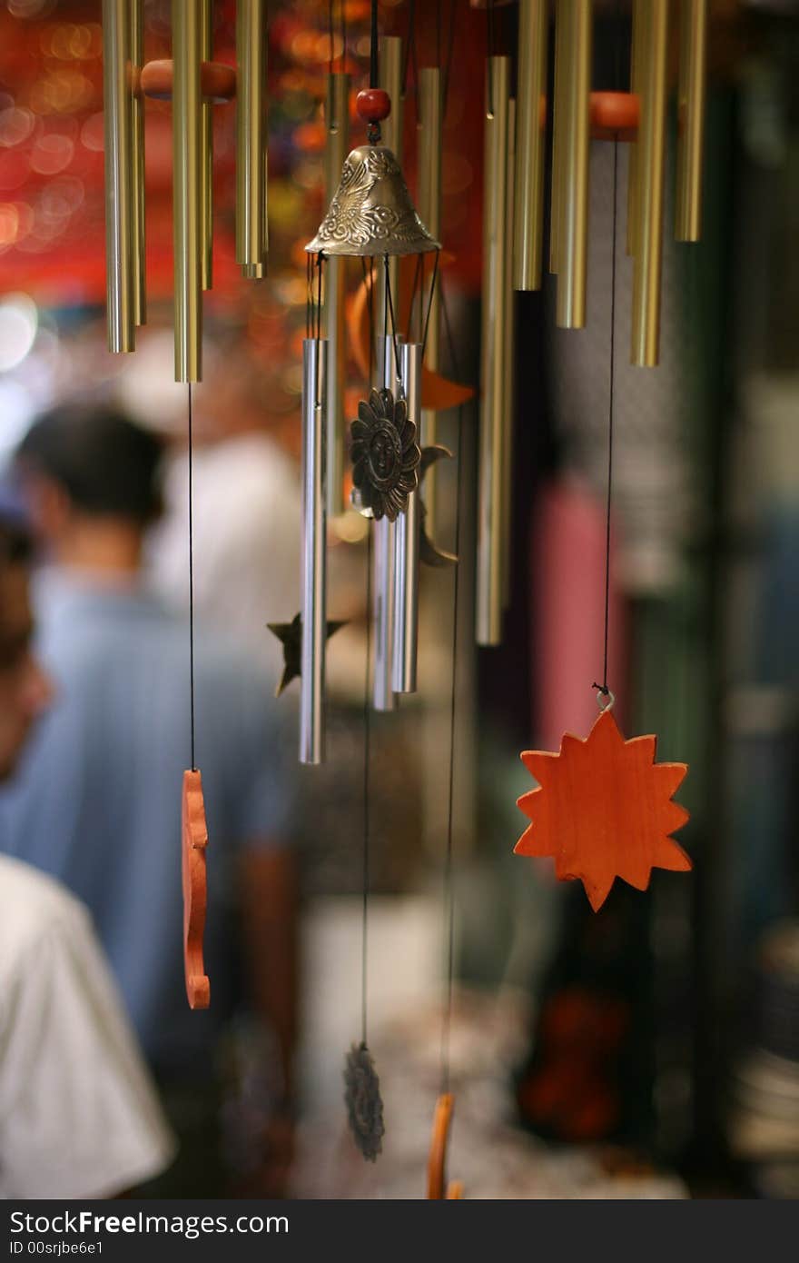 Close up of wind bells,three metal bells, orange sun decoration, blury background of pepole walking in the market. Close up of wind bells,three metal bells, orange sun decoration, blury background of pepole walking in the market