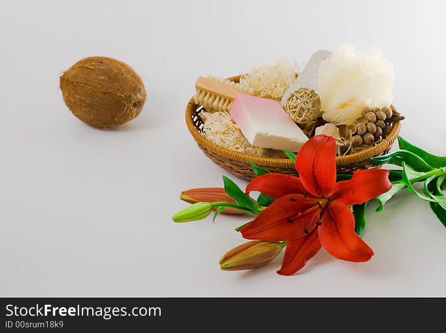 Personal care items and decorations in a basket, a coconut and a red lily isolated on white background.