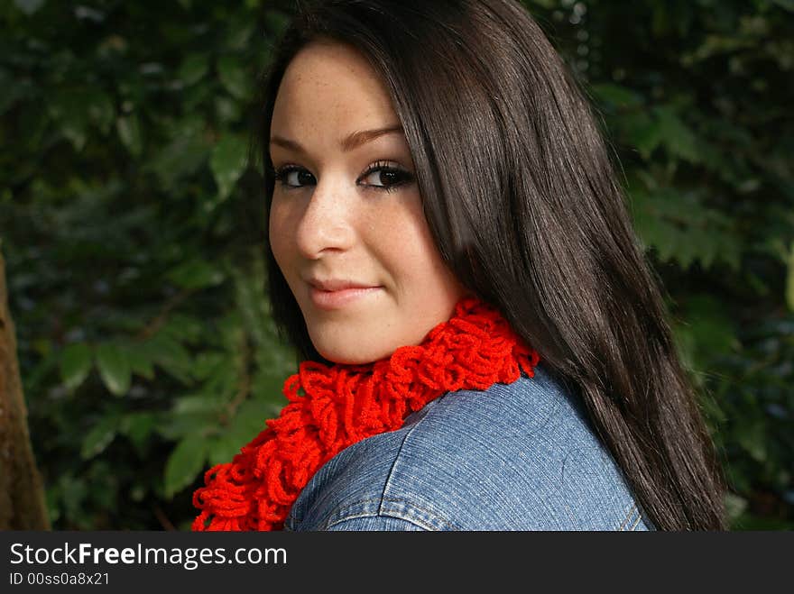 Close-up of girl wearing red scarf and coy expression isolated against wooded background. Close-up of girl wearing red scarf and coy expression isolated against wooded background