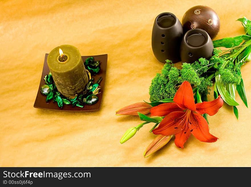 Red lily, green scented candle and black oil burner on golden background. Red lily, green scented candle and black oil burner on golden background.