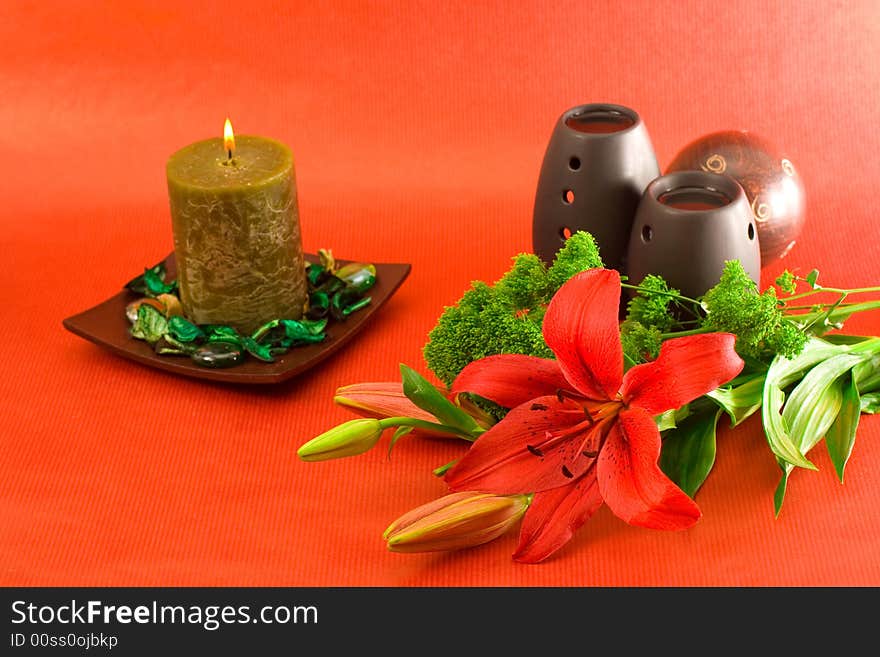 Red lily, red scented candle and black oil burner on red background. Red lily, red scented candle and black oil burner on red background.