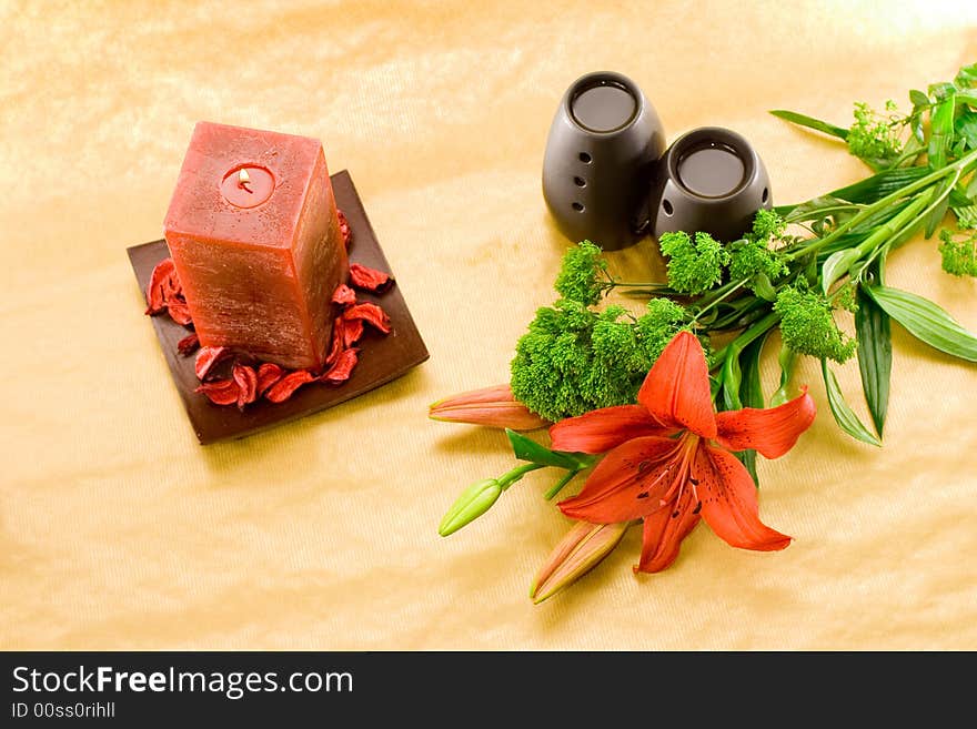 Red lily, red scented candle and black oil burner on golden background. Red lily, red scented candle and black oil burner on golden background.