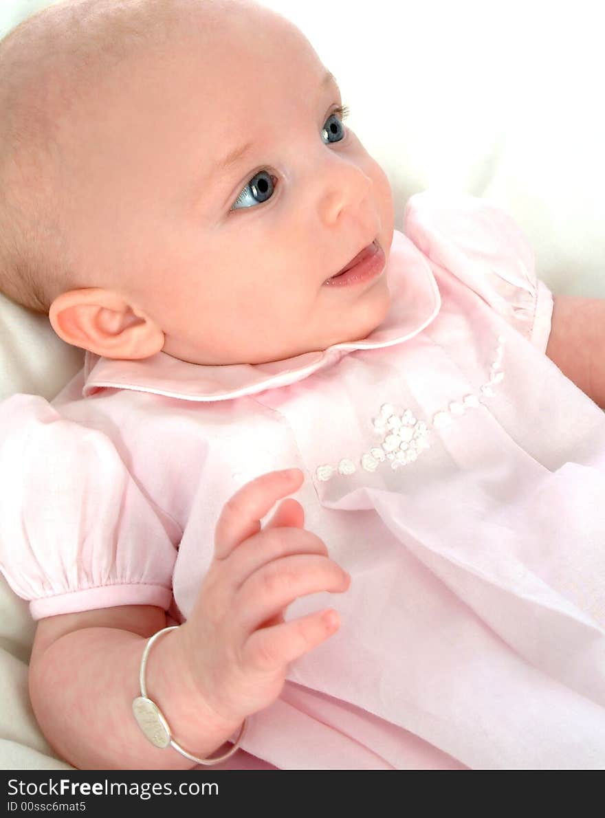 Smiling baby girl in pink dress on white comforter. Smiling baby girl in pink dress on white comforter