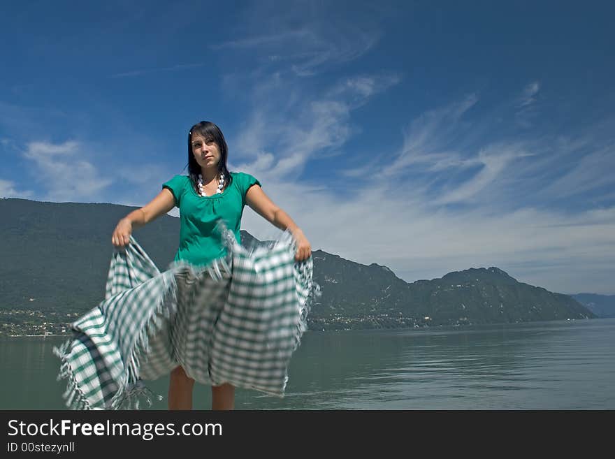 Woman extending a tablecloth for a picnic at the edge of a lake