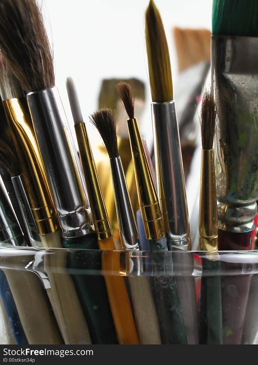 Close-up shot of a glass full of messy, used paint brushes against a light background. Close-up shot of a glass full of messy, used paint brushes against a light background