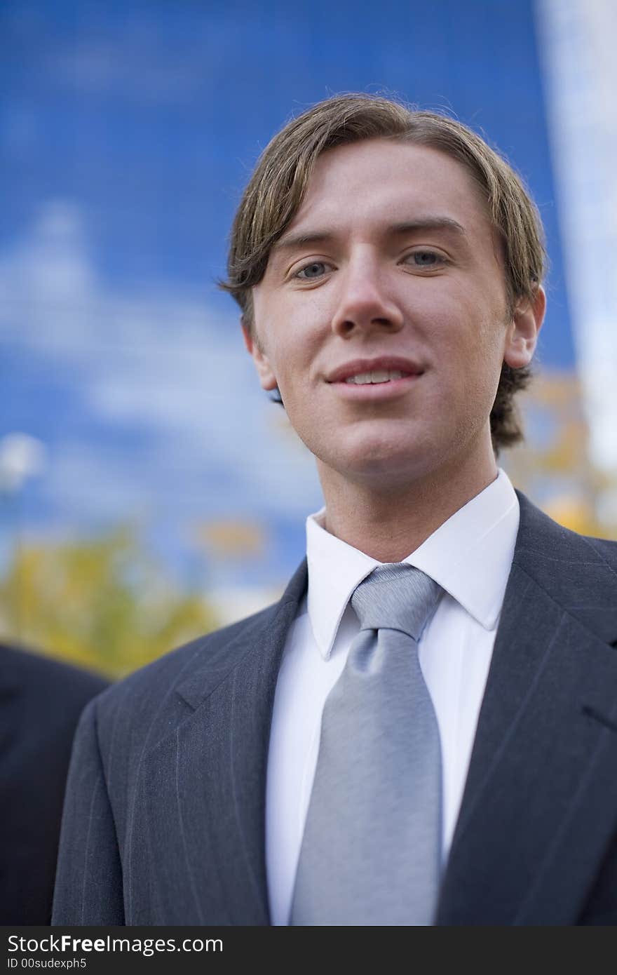 Close front view of single white businessman in suit in front of blue office building. Close front view of single white businessman in suit in front of blue office building