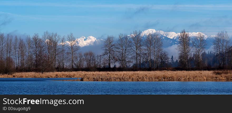 The Cascade Mountains in winter snow as seen across Shadow Lake at the Bob Heirman Wildlife Preserve in Snohomish, WA.