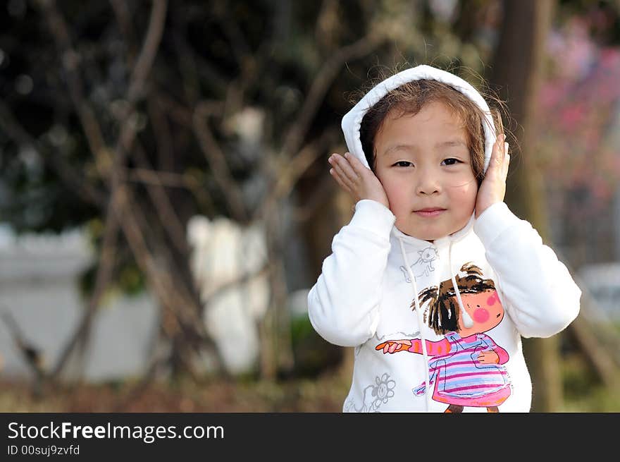 The cute little girl is touching her red face by her small hands.