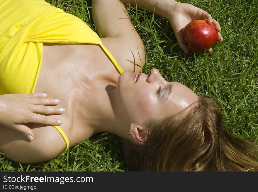 Young tanned woman resting on the grass with red apple. Young tanned woman resting on the grass with red apple