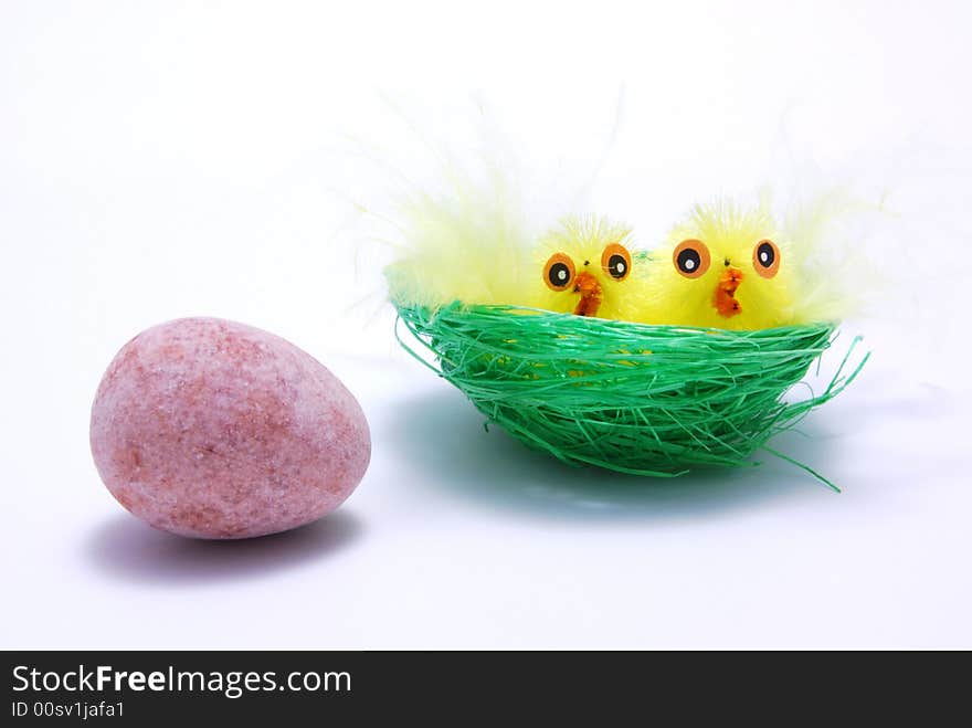 Two easter chicks in a nest with an egg outside