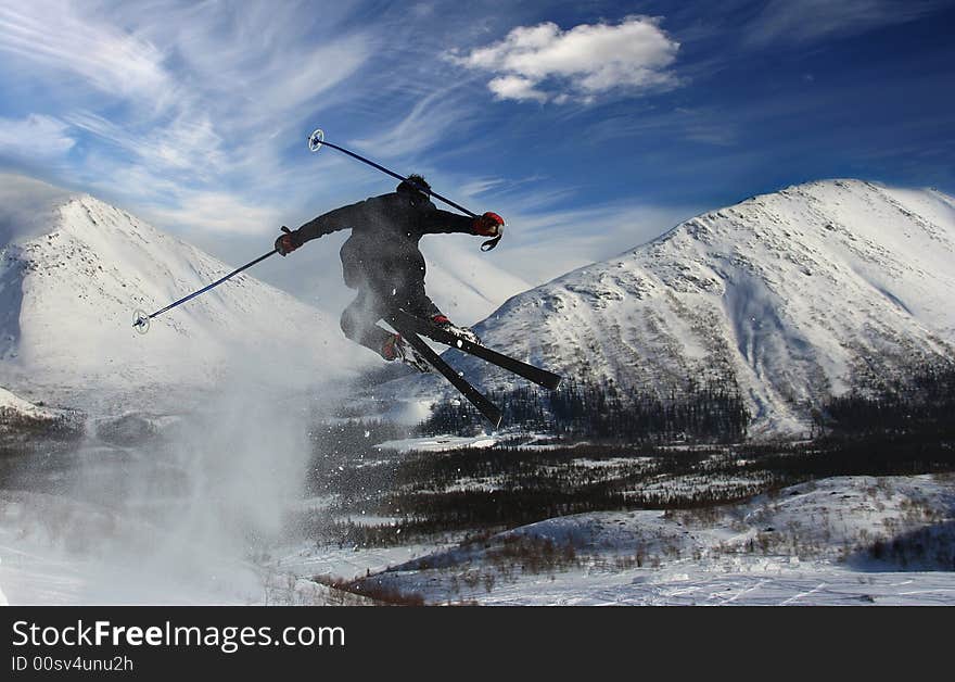 The skier in mountains in flight from a back